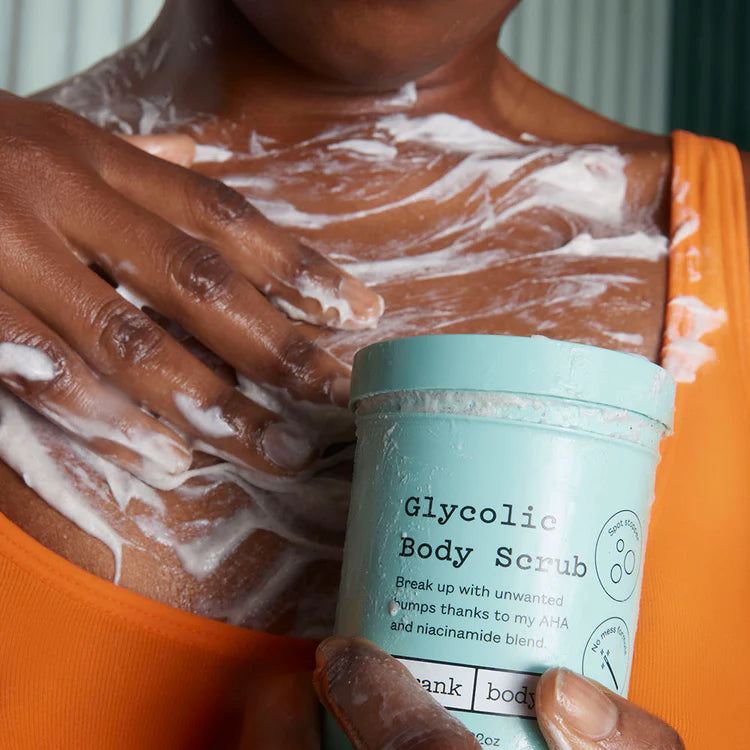 Eine Person trägt das weiße FRANK BODY Glycolic Body Scrub auf die Haut auf und hält dabei den mintgrünen Tiegel