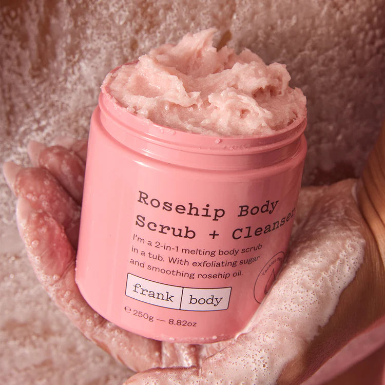 Geöffnete rosa Dose FRANK BODY Rosehip Body Scrub + Cleanser in schäumenden Händen mit pastöser Peeling-Textur