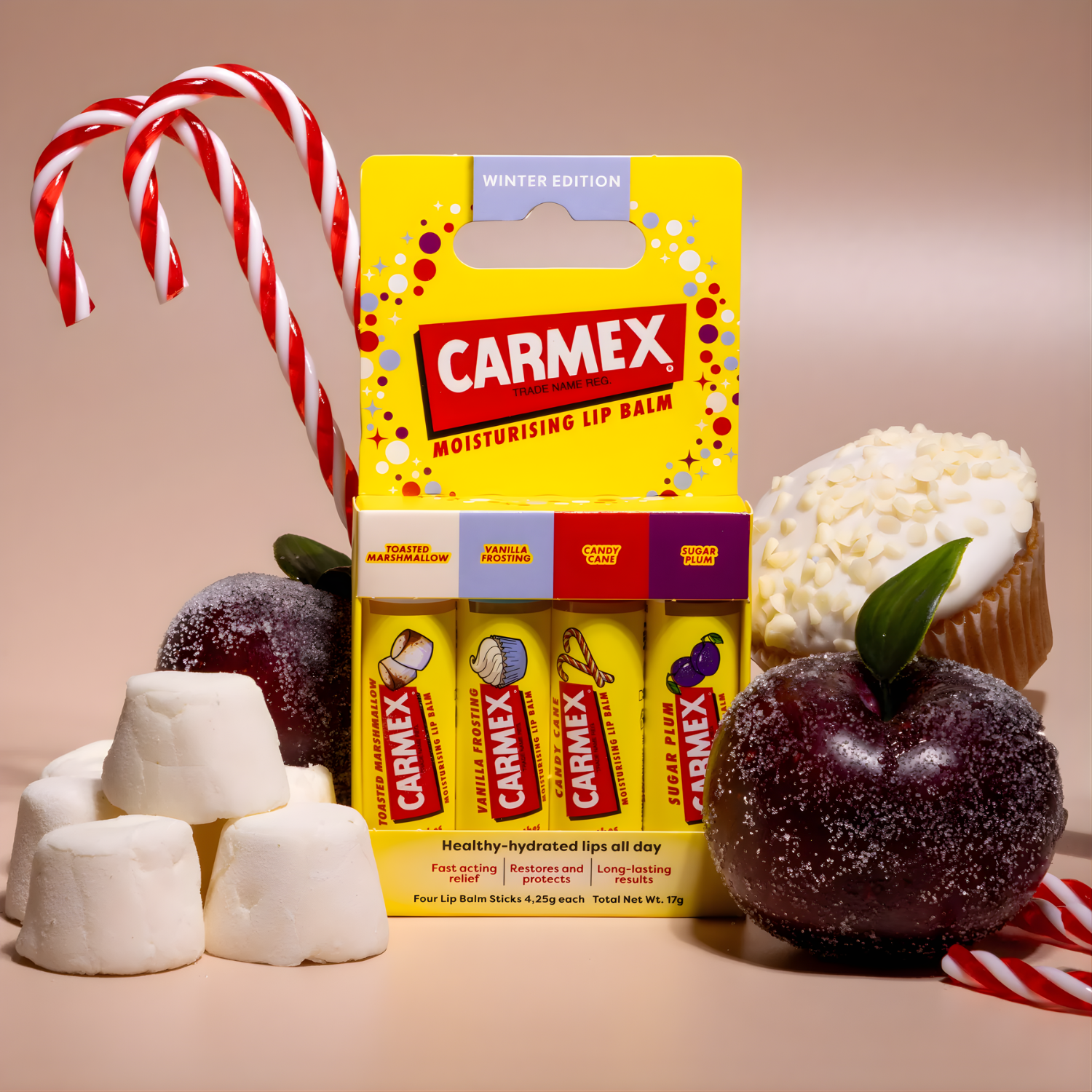 Eine Winteredition von Carmex Lippenbalsam, umgeben von Süßigkeiten wie Zuckerstangen, Marshmallows, einer Pflaume und einem Cupcake.